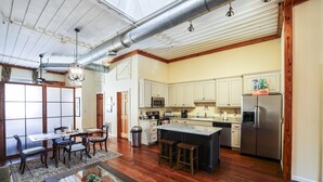 Une cuisine spacieuse avec un plancher en bois, un coin repas avec une table et des chaises, et un grand îlot central avec des tabourets.
