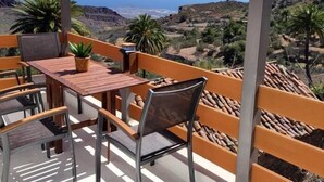 A balcony with a wooden table and chairs, overlooking a coastal landscape with hills and a view of the sea. - Natural beauty at Sol Caldera de Temisas (Temisas)