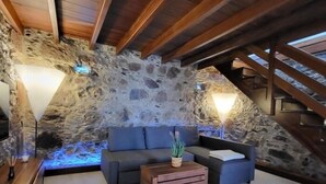 A cozy loft bedroom with a stone wall, a wooden staircase, a gray sofa, and a small wooden table. - Natural beauty at Sol Caldera de Temisas (Temisas)