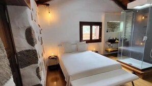A bedroom with a large bed, bedside tables, a window, and a glass shower enclosure. - Natural beauty at Sol Caldera de Temisas (Temisas)