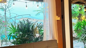 Una habitación con techo de madera, un sofá, una ventana con cortina y vistas al exterior con vegetación.
