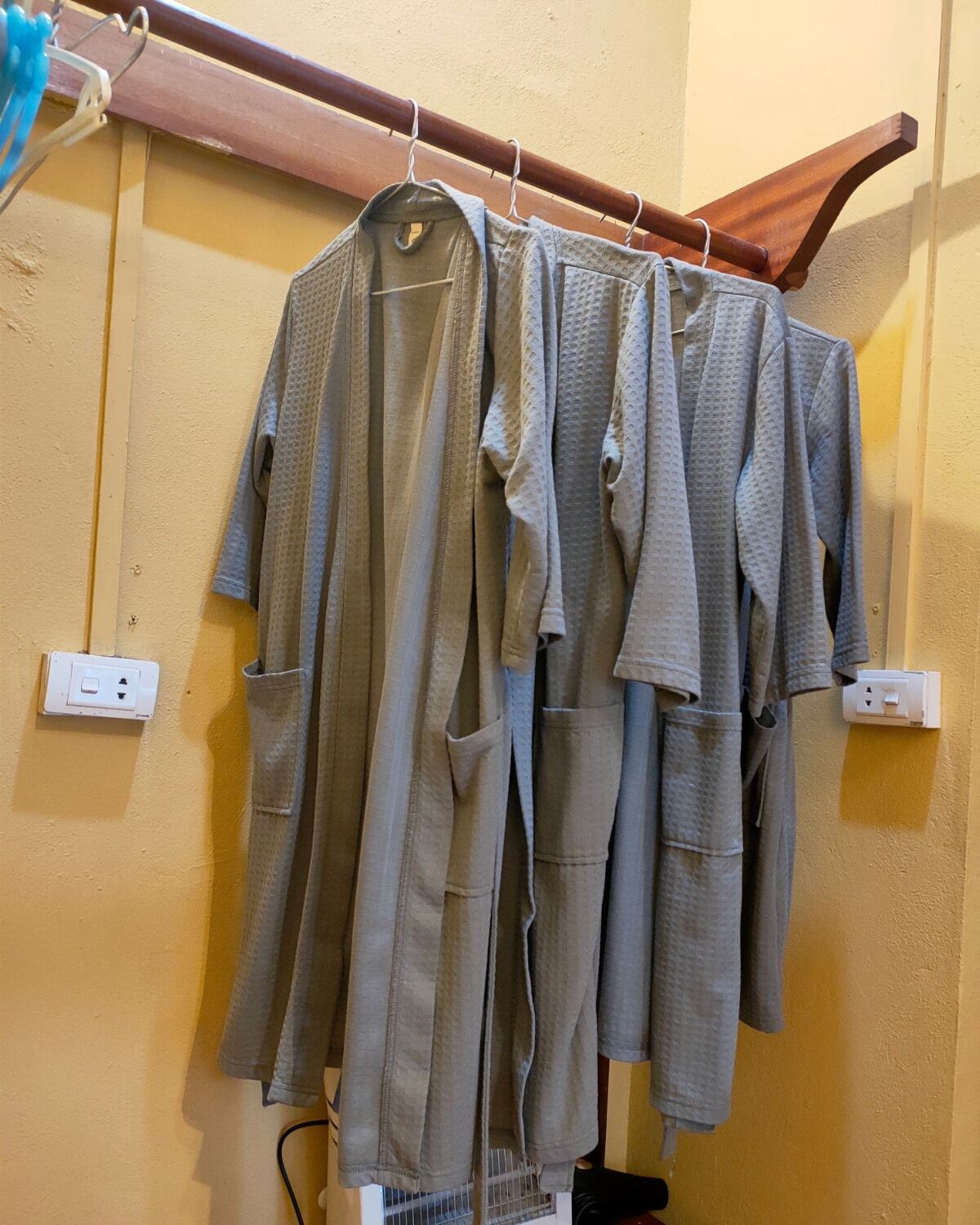 A rack with multiple grey robes hanging against a yellow wall.