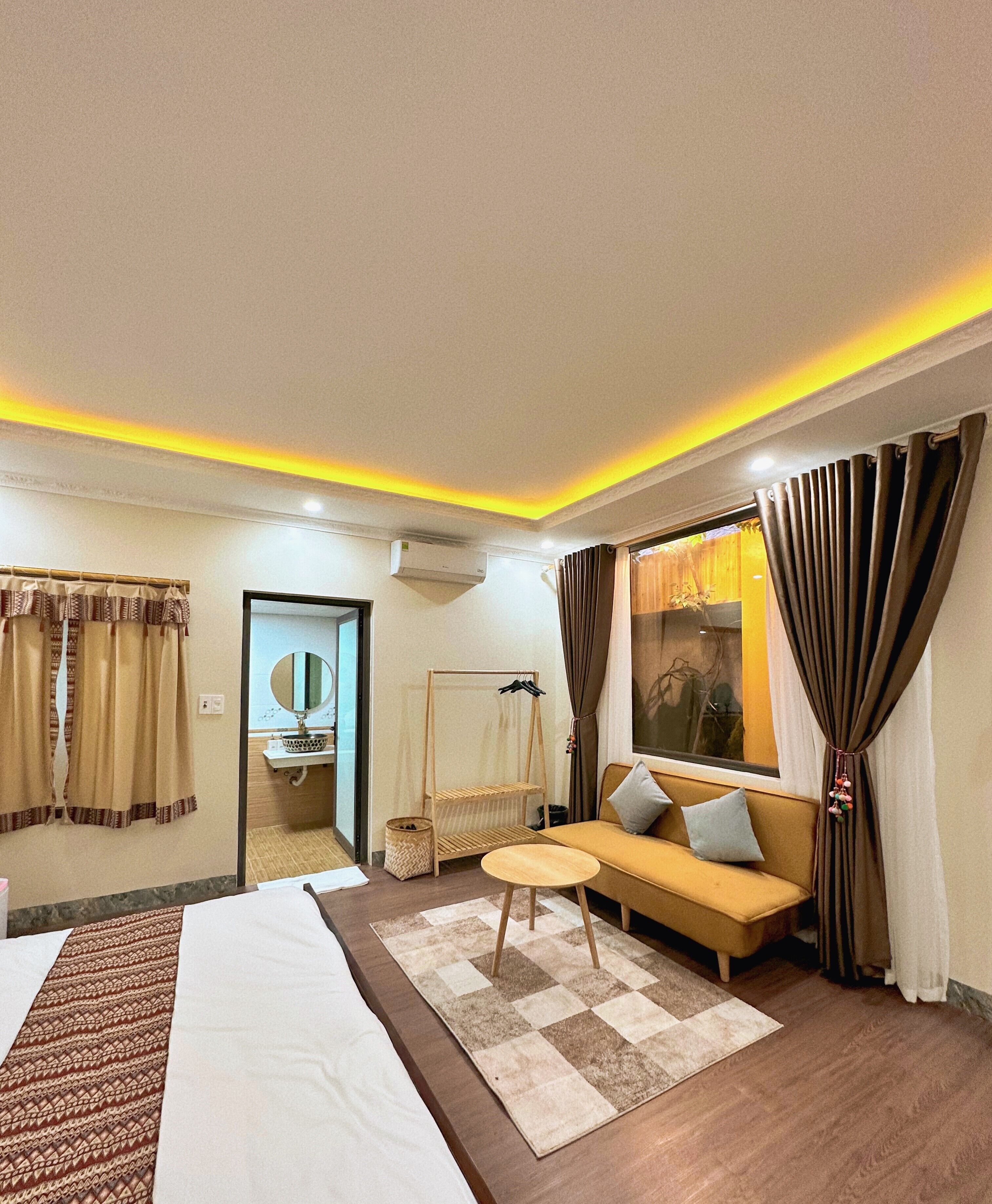 Une chambre d’hôtel avec un lit, un canapé, une petite table et une fenêtre avec des rideaux.