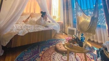 A room with a wooden ceiling, a bed with a canopy, a hammock, and a patterned rug.