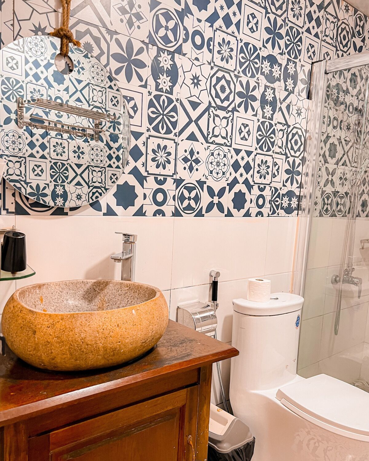 A bathroom with a large, round, beige ceramic sink, a wooden vanity, a glass shower enclosure, and a toilet with a white lid.