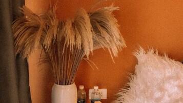 A bedside table with a vase of dried pampas grass, three candles, and a bottle of water.