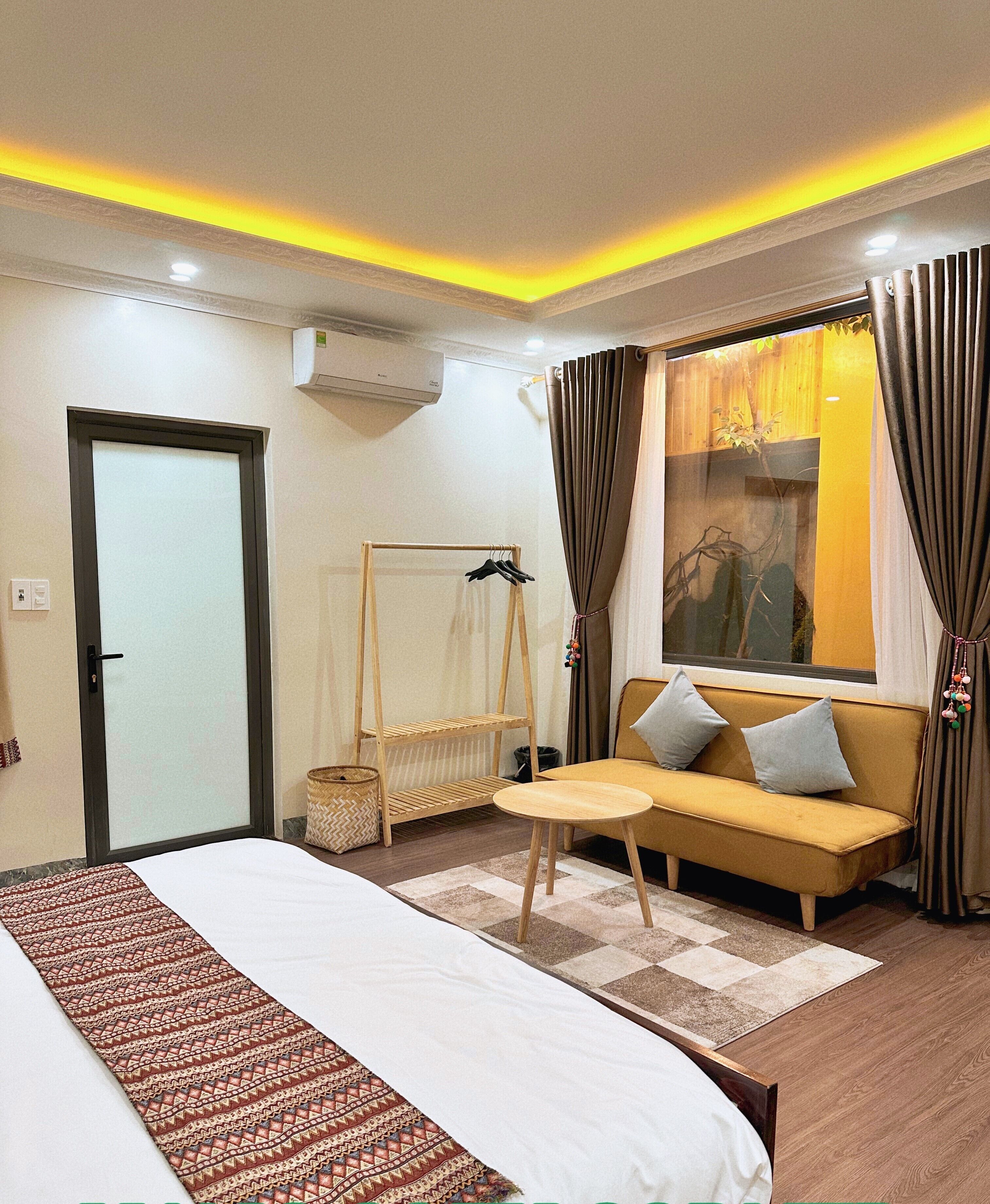 Een moderne hotelkamer met een bed, een bank, een klein tafeltje en een raam met gordijnen.