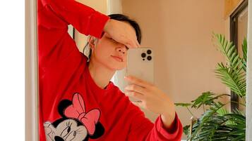 A person taking a selfie in a room with wooden ceiling, a white wall, and a potted plant.