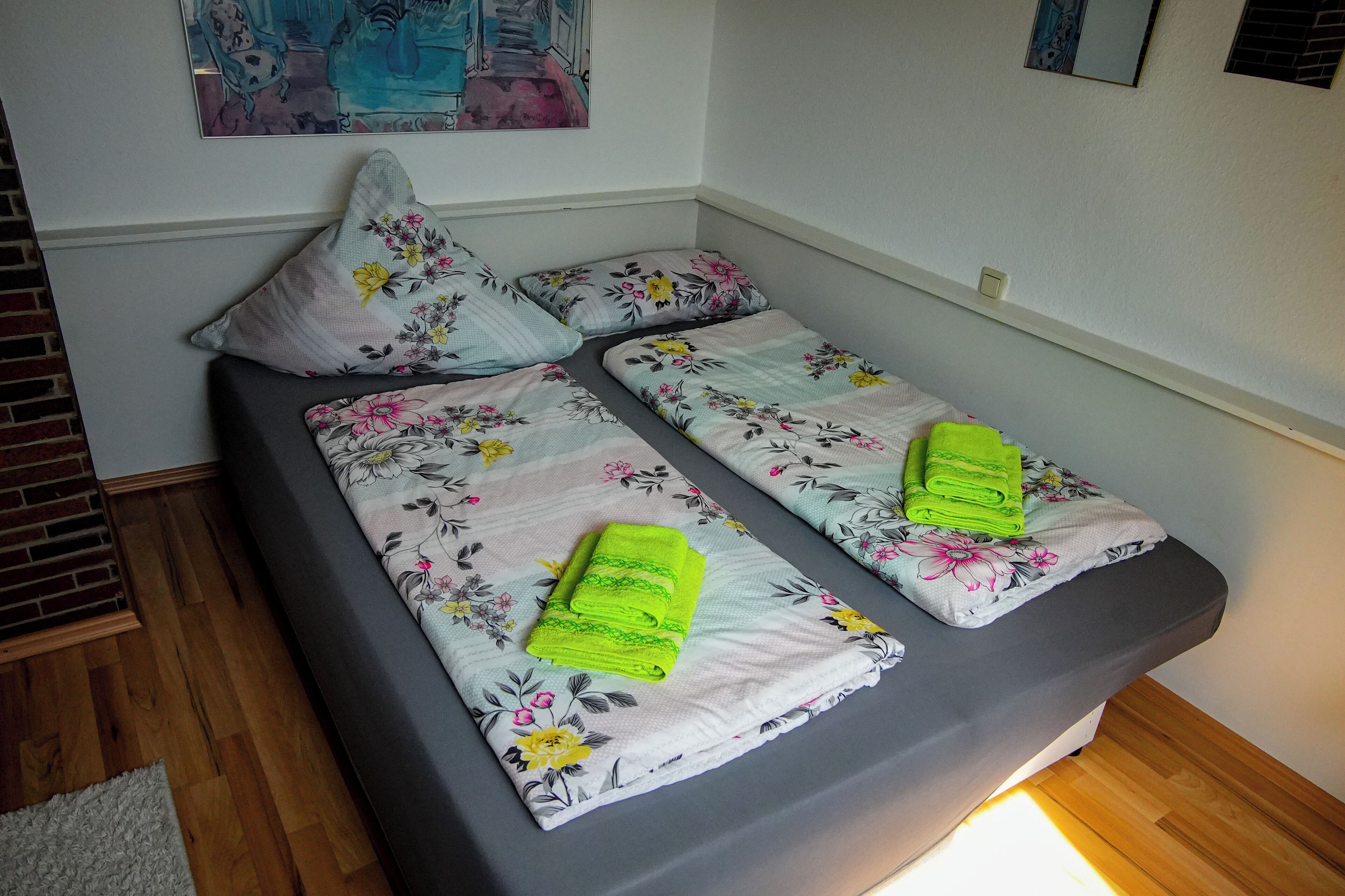 A double bed with floral bedding and two bright green towels.