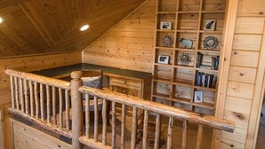 Een houten interieur met een trap, een houten leuning en een wand met planken vol decoratieve objecten.