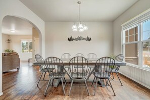 A dining area with a long table, six chairs, and a chandelier. - Mountain Breeze! Fire Pit, Air Hockey & Views! (Monument)