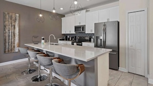 A modern kitchen with white cabinets, a stainless steel refrigerator, and a central island with bar stools.