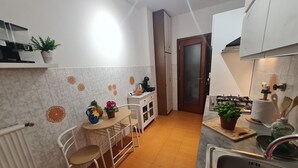 A compact kitchen with white cabinets, a tiled backsplash, and a small dining area with a table and chairs. - Villa Christele Sanremo (Sanremo)