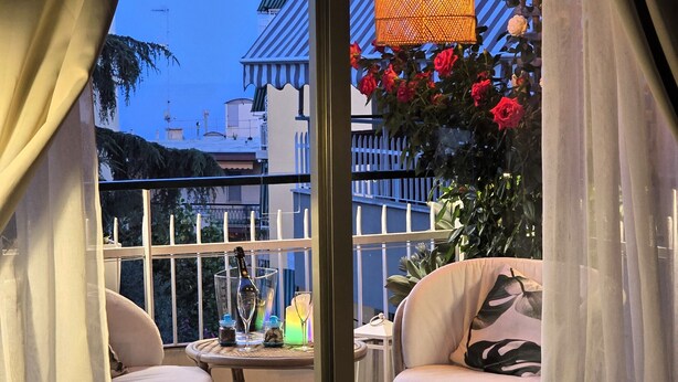 A balcony with two chairs, a table with a bottle and glasses, and hanging lamps. - Villa Christele Sanremo (Sanremo)