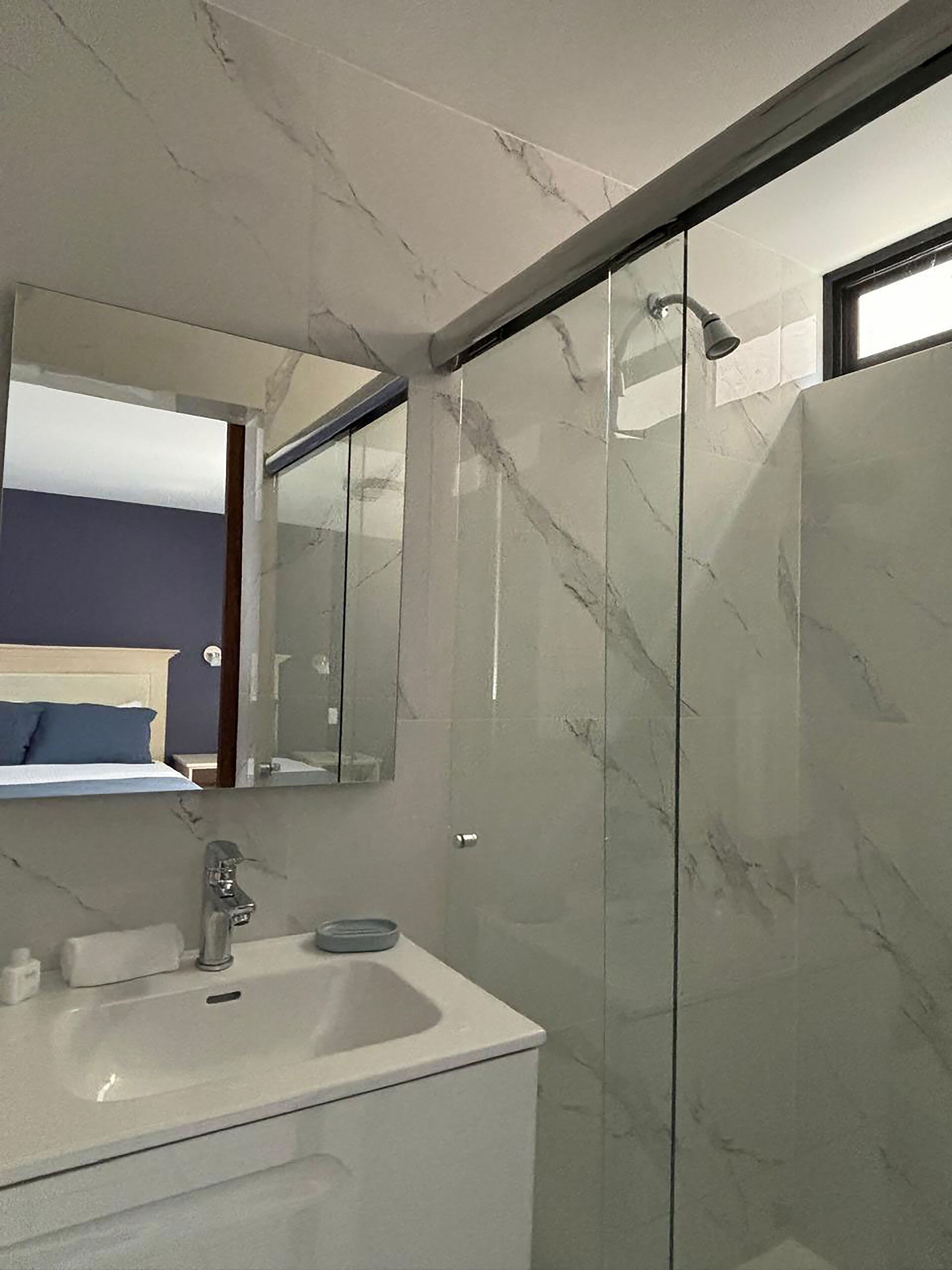 Un baño moderno con lavamanos de mármol, cabina de ducha con paredes de vidrio y un espejo grande.