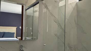Un baño moderno con lavamanos de mármol, cabina de ducha con paredes de vidrio y un espejo grande.