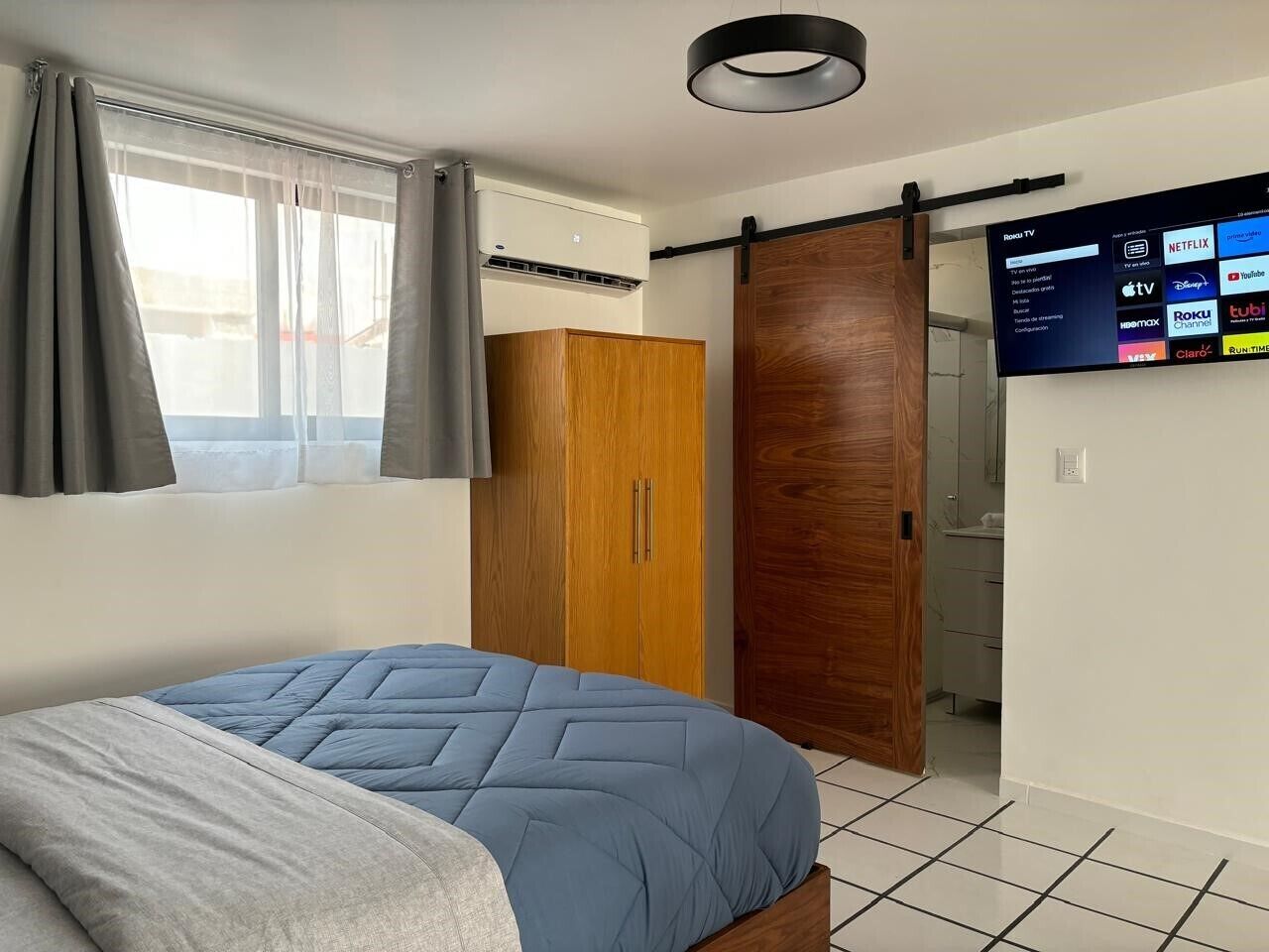 Ein Schlafzimmer mit Bett, Kleiderschrank, Schiebetür, Fernseher und Deckenleuchte.