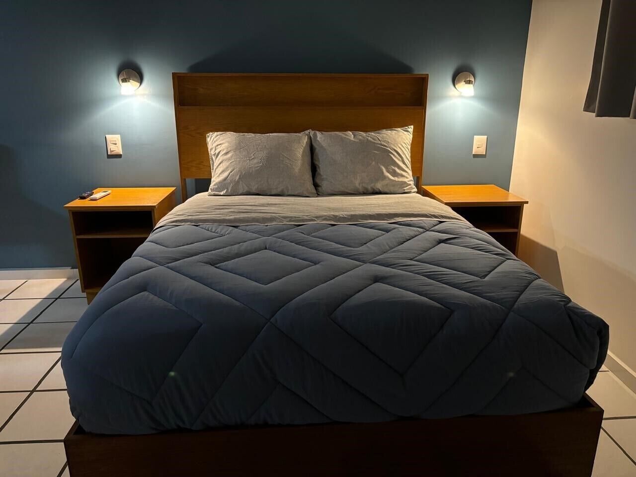 A bed with a quilted cover, two bedside tables, and wall-mounted lights.