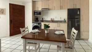 A compact kitchen with a microwave, oven, and refrigerator. There is a dining table with chairs and a small potted plant.