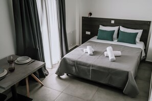 A neatly arranged hotel room with a bed, a table with a plate and glasses, and a window with curtains.