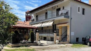 A two-story building with a balcony, a small attached structure, and a car parked in front. - Crystal Studios (Aristotelis)