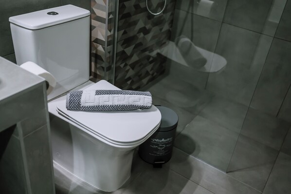 A modern bathroom with a toilet, a trash bin, and a patterned towel. - Crystal Studios (Aristotelis)