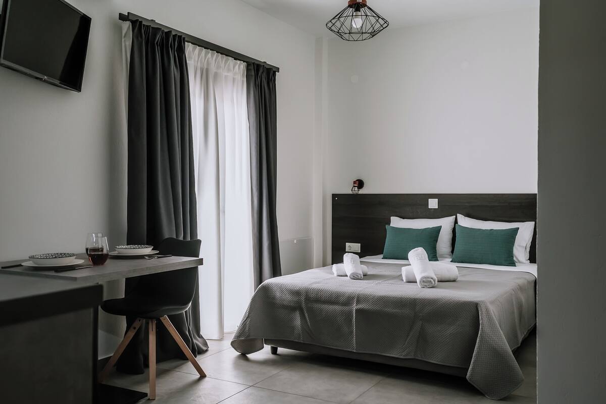 Une chambre d’hôtel moderne équipée d’un lit, d’un bureau avec une chaise, d’un téléviseur fixé au mur et d’une fenêtre avec des rideaux.