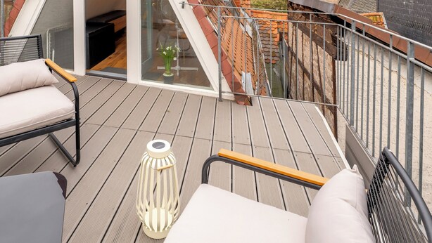 Terraza en la azotea con puerta de vidrio que da a un espacio interior, amueblada con un sofá y sillas, y una lámpara decorativa.