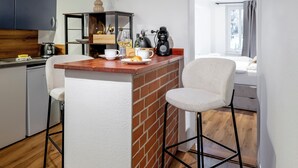 Una cocina compacta con una isla central, dos taburetes de bar, una cafetera y un jarrón con flores.