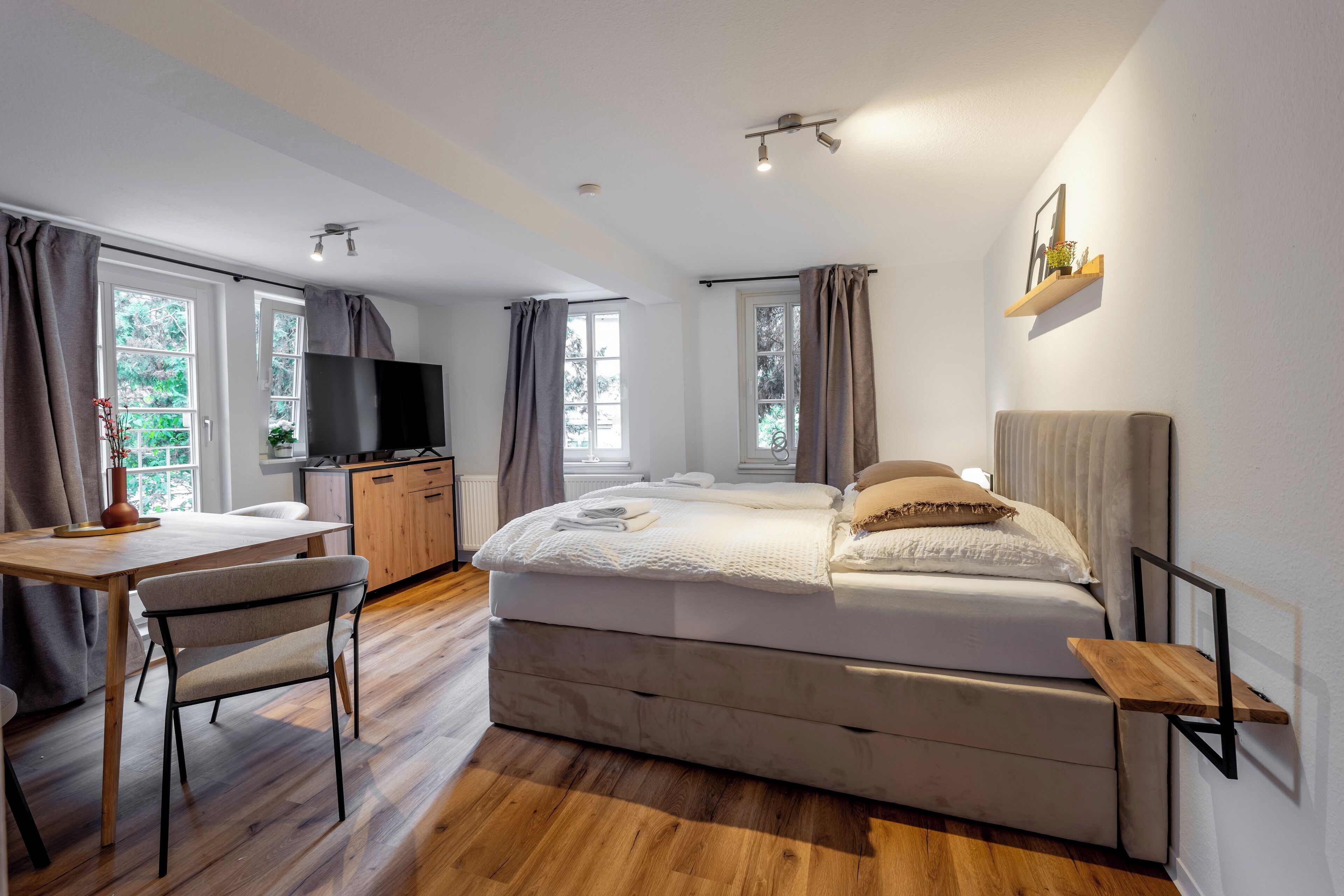 A modern bedroom with a bed, bedside tables, a TV, and a desk.