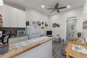 A compact living space with a kitchenette, a ceiling fan, a TV, and a sofa.