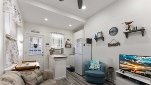 Un espacio habitable compacto con kitchenette, un sofá, un televisor y elementos decorativos en la pared.