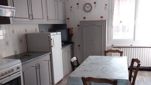 Una cocina con armarios blancos, una mesa de comedor con sillas, un reloj en la pared y una ventana con cortinas.