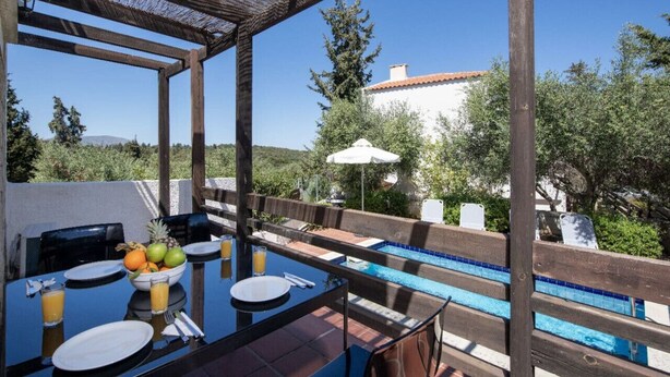 A poolside dining area with a table set for two, a bowl of fruit, and a glass of orange juice. - Villa Olivia - a compund villa witha  private pool (Douliana)