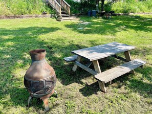 Entorno rústico al aire libre con una mesa de picnic de madera y una parrilla de metal.