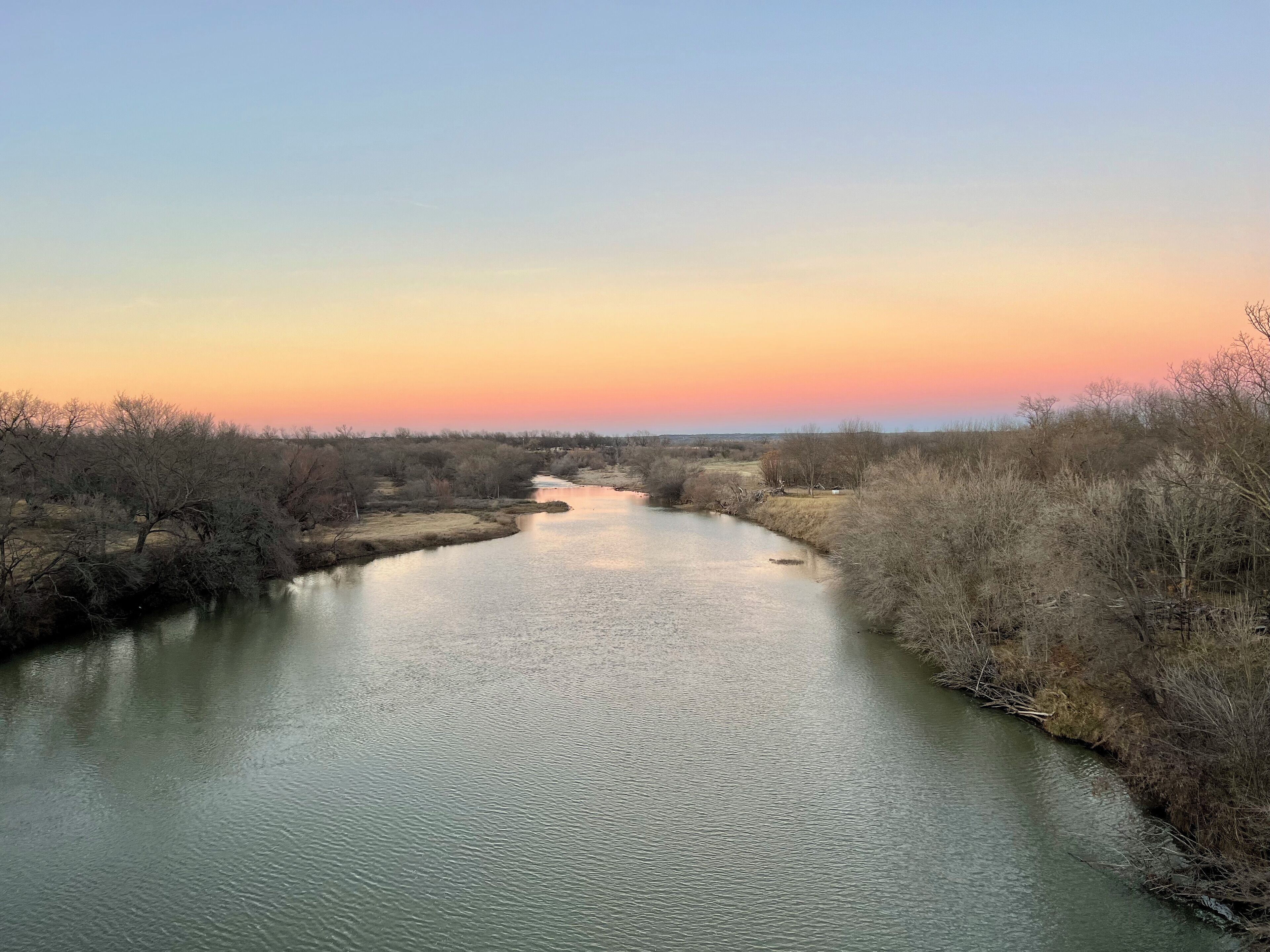 Un río serpentea por un paisaje de vegetación escasa bajo un cielo despejado.