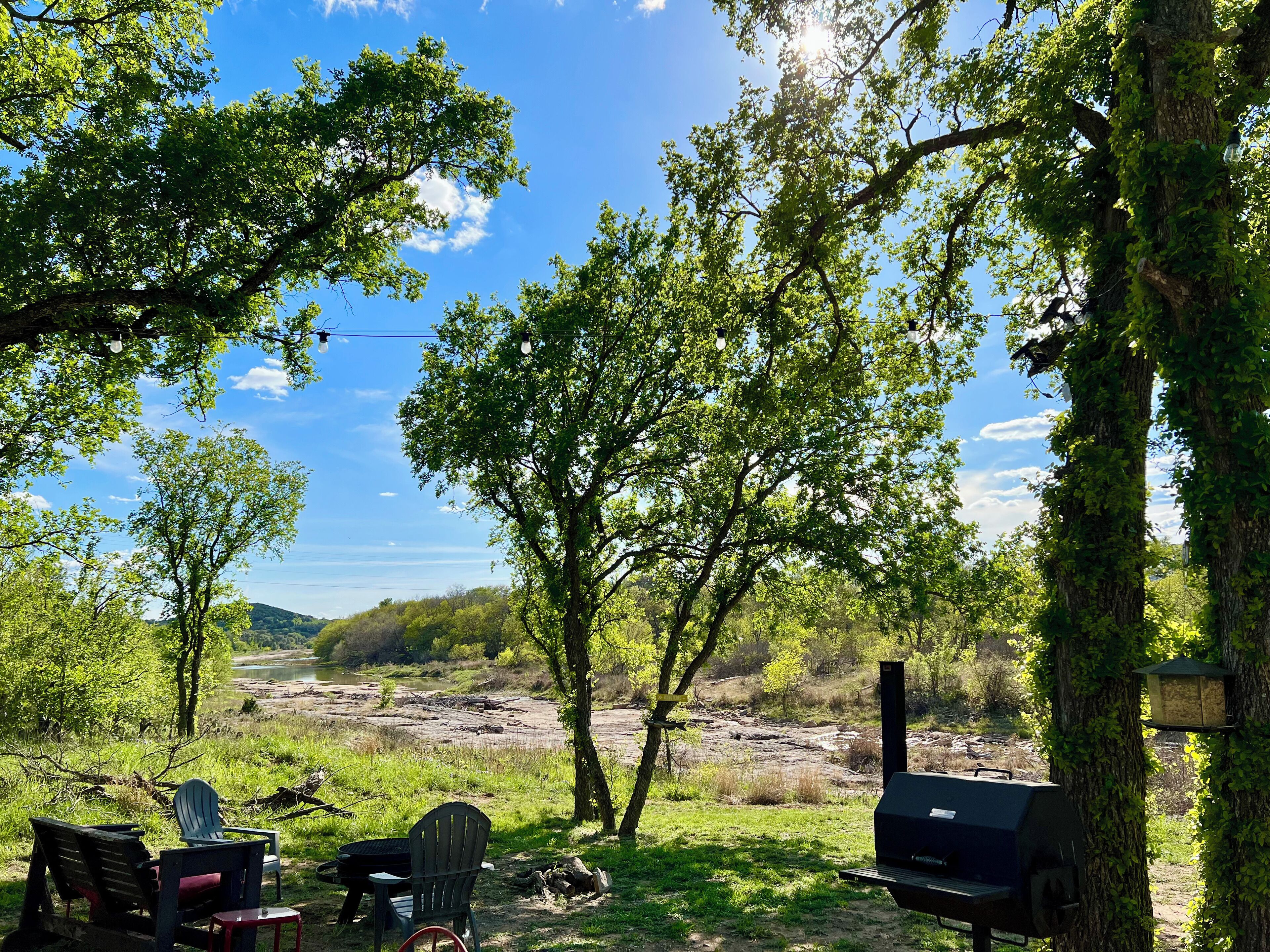 Een camping met Adirondack stoelen, een barbecue en uitzicht op een rivier en heuvels.