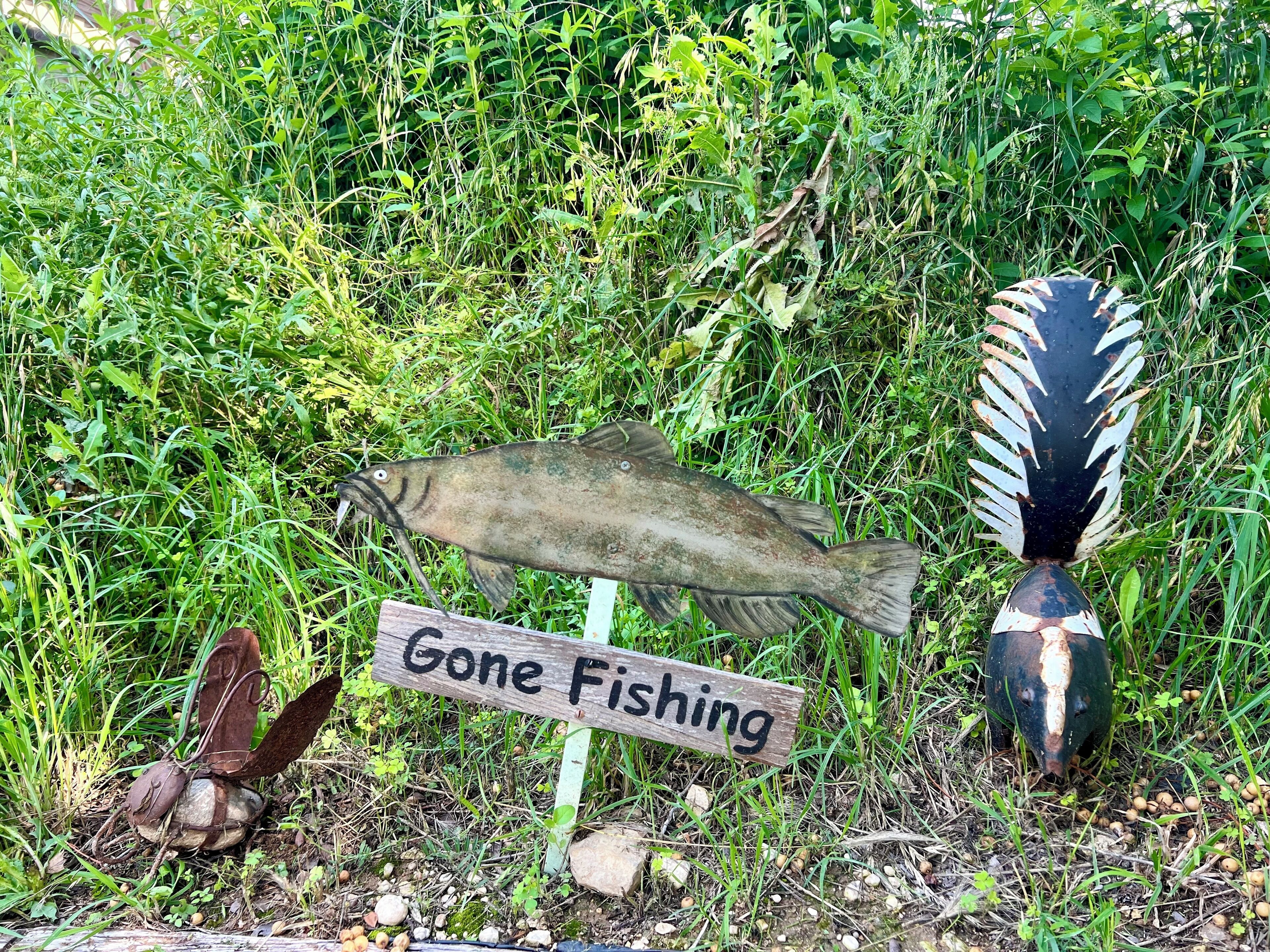 Een houten bordje met de tekst ‘Gone Fishing’ in een natuurlijke omgeving met gras en een vis.