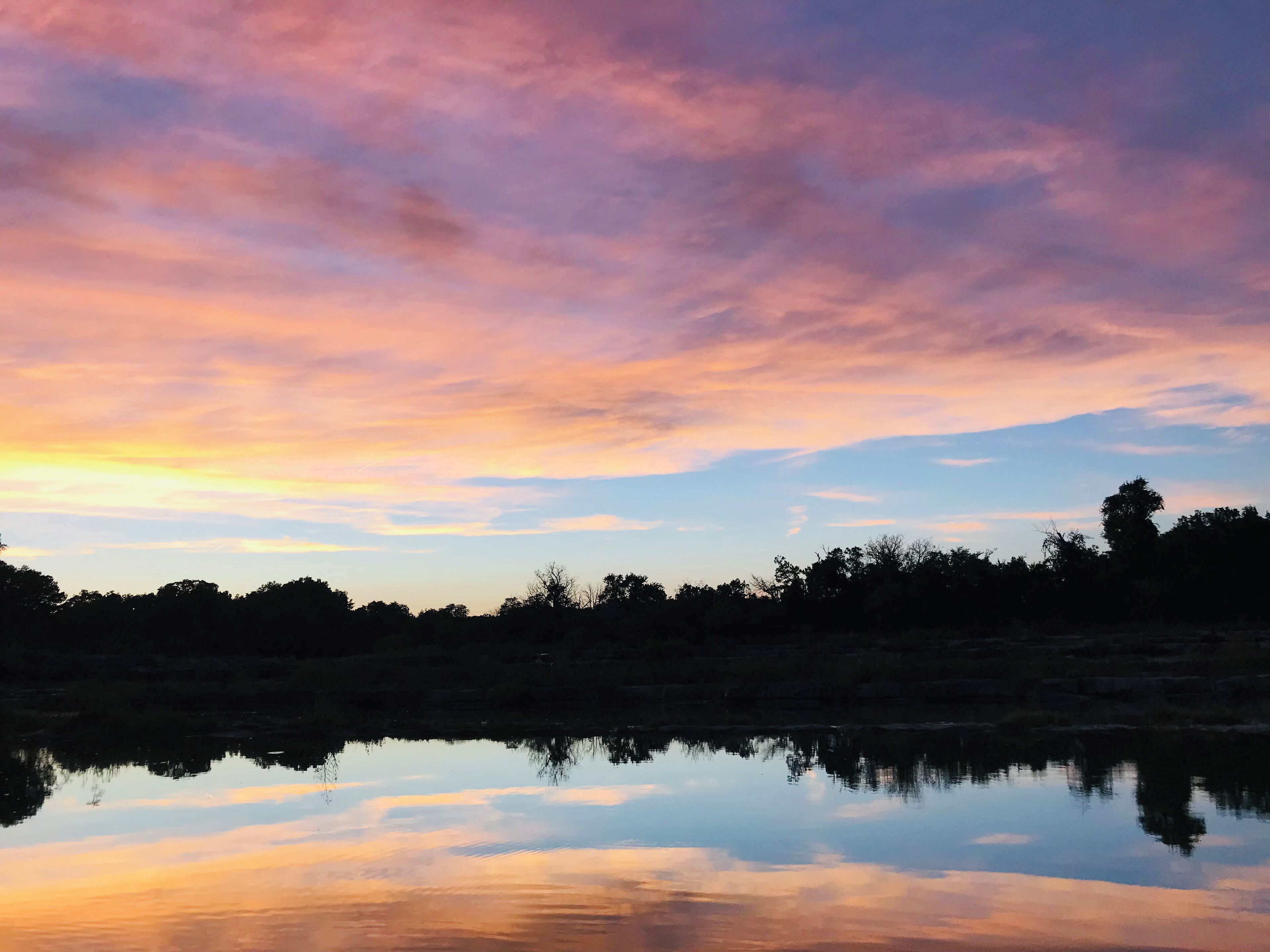 A sunset over a calm body of water with a silhouette of trees in the foreground.