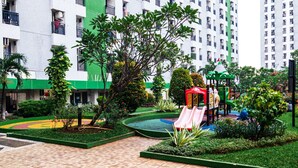 A playground with a slide and climbing structures, surrounded by well-maintained greenery and a tiled walkway.
