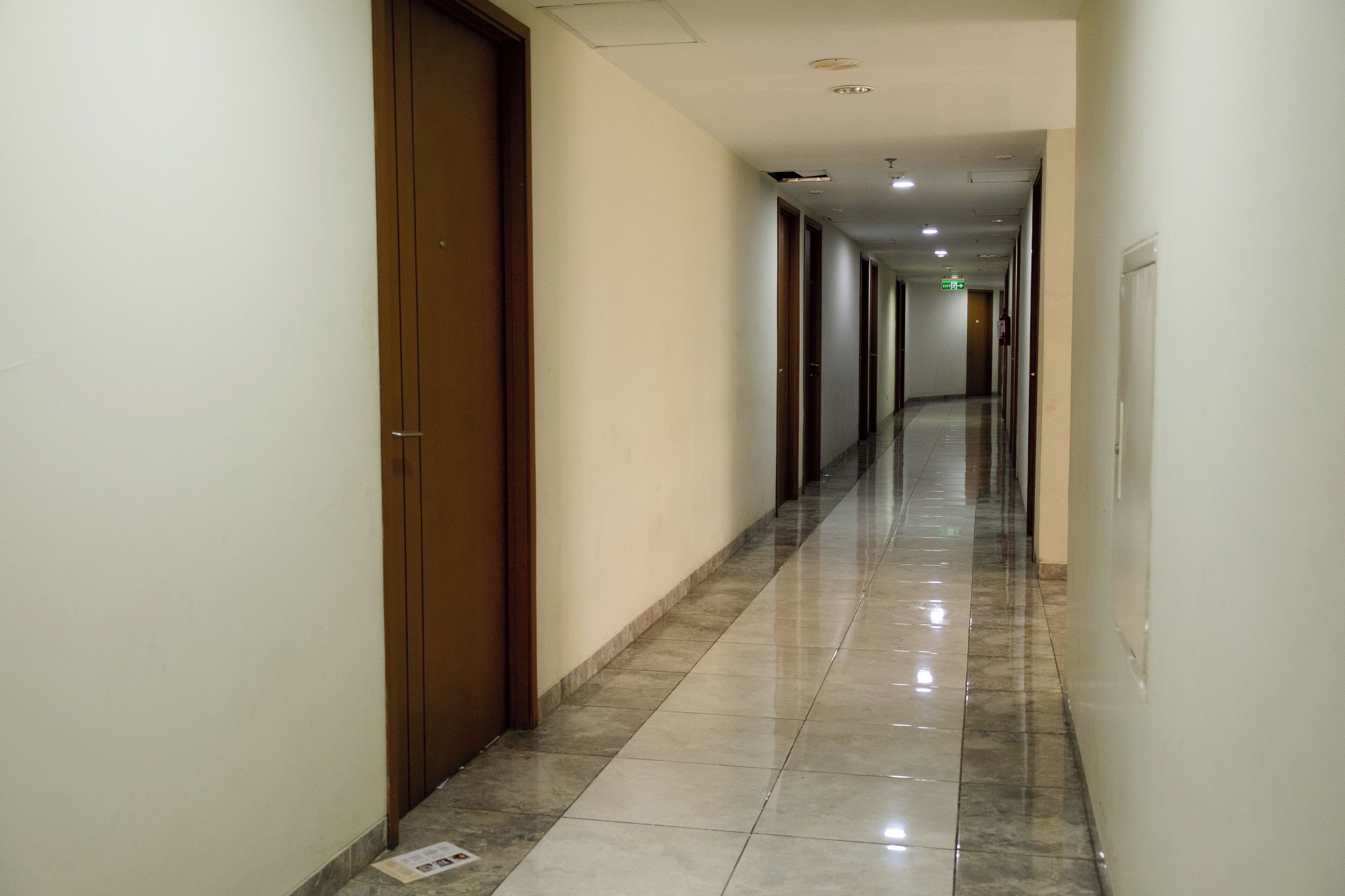 Un largo pasillo estrecho con piso de baldosas brillantes y puertas de madera a un lado.