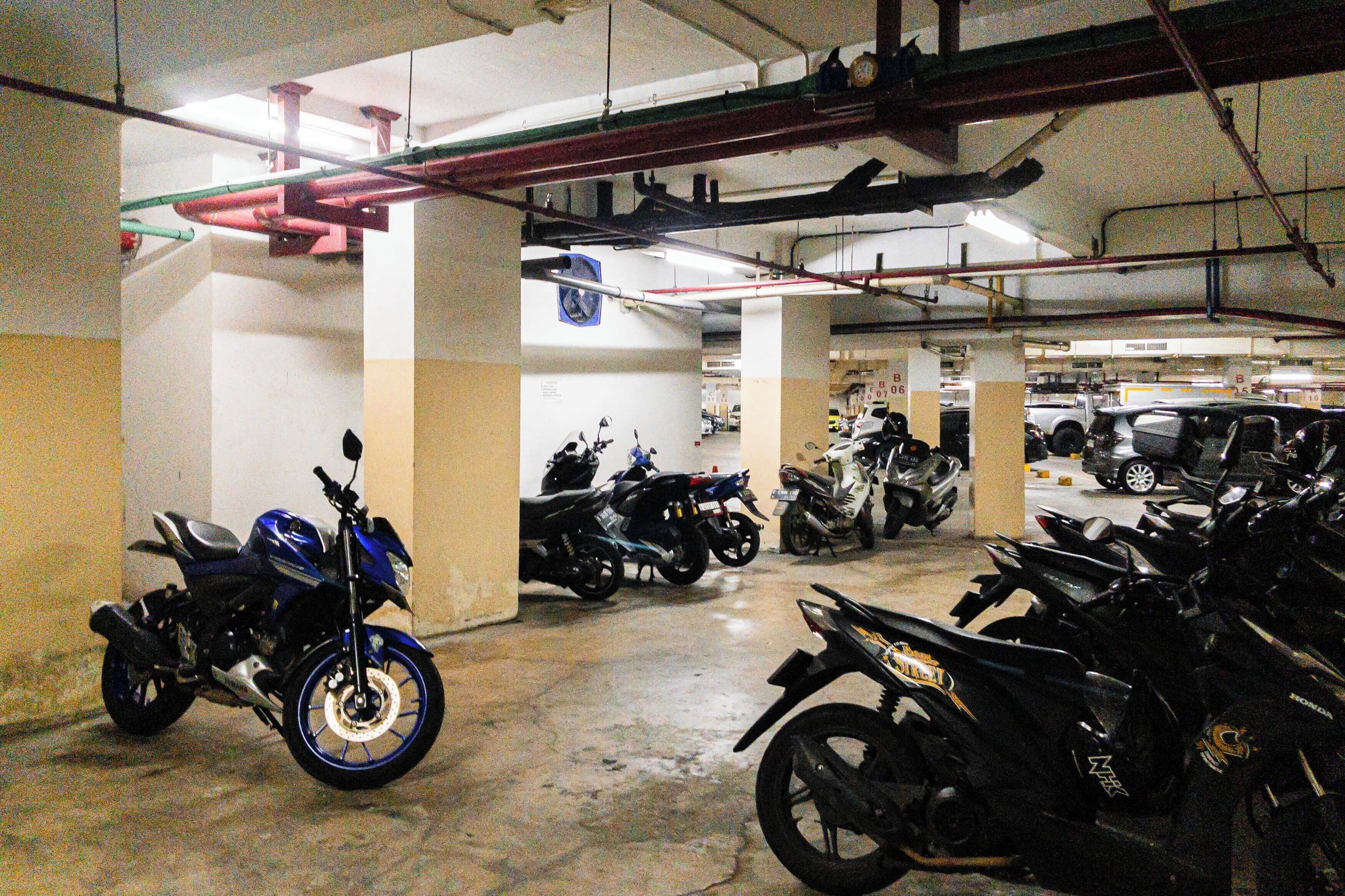 A parking garage with multiple motorcycles and cars parked.