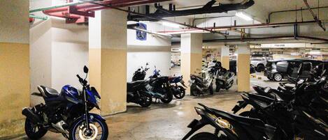 A parking garage with multiple motorcycles and cars parked.