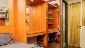 A bedroom with a bed, a wooden wardrobe, a mirror, and a door with curtains.