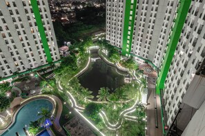 A high-rise building with a landscaped courtyard featuring a pond and palm trees, surrounded by illuminated pathways. - Pelangi Rooms By Reccoma (South Tangerang)
