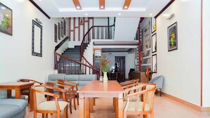 Amplia sala de estar con una mesa de comedor de madera, sillas, sofás y una escalera que conduce a un nivel superior.
