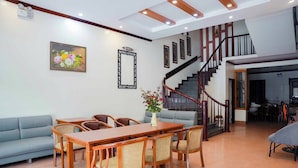 Amplia sala de estar con una mesa de comedor de madera, un sofá azul y una escalera que conduce a un piso superior.