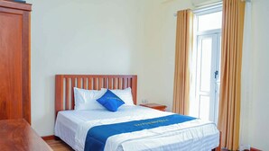 Una cama bien tendida con un almohadón azul y una colcha, una mesita de noche de madera y un armario de madera.