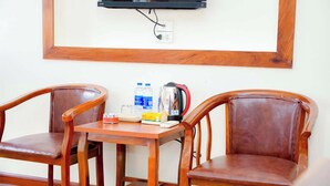 Una habitación con dos sillas de madera, una mesita, un televisor montado en la pared y un enchufe.