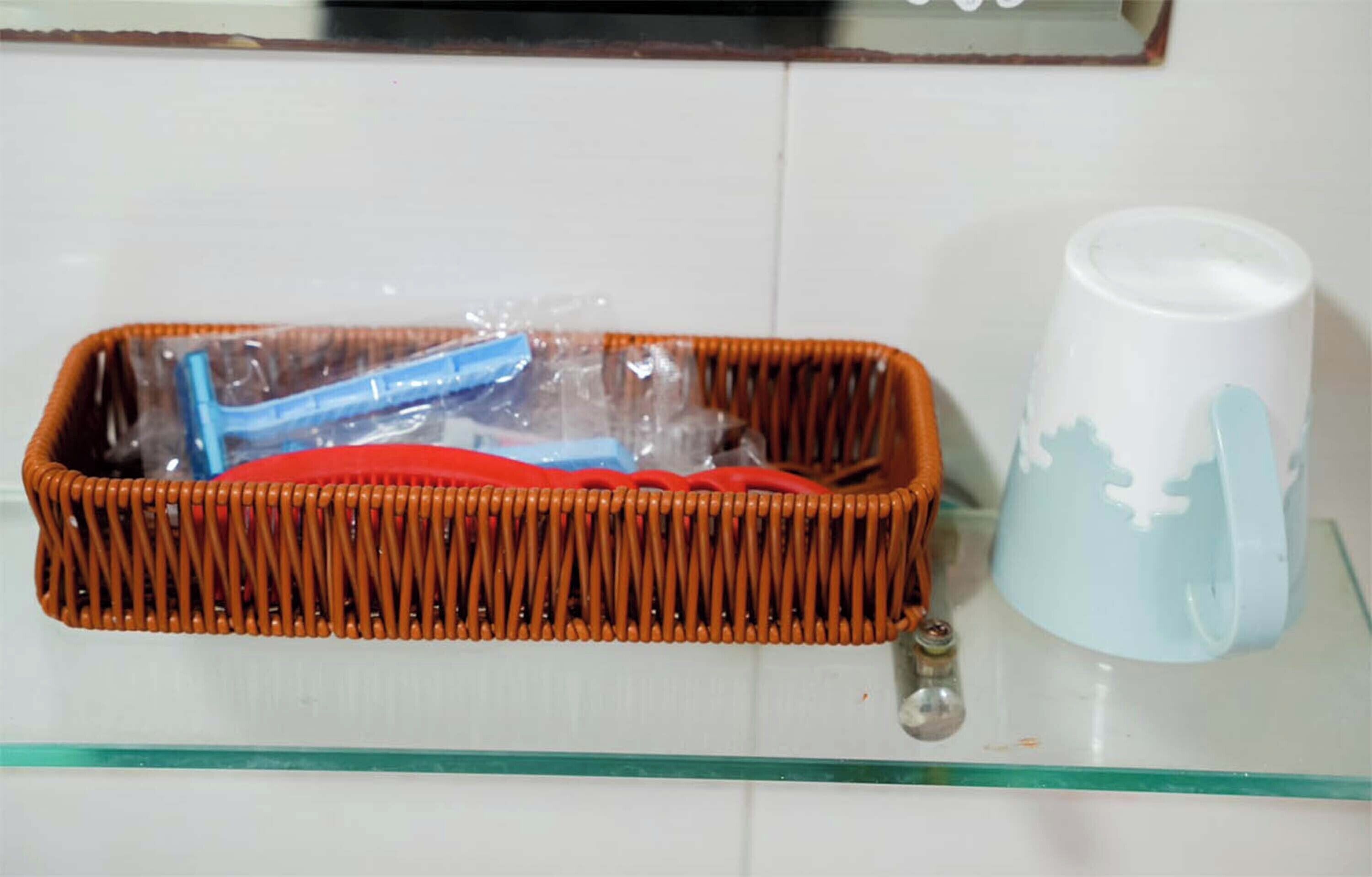 Una cesta de mimbre con interior rojo y un objeto azul en su interior, sobre un estante de vidrio junto a una taza blanca con un diseño azul.